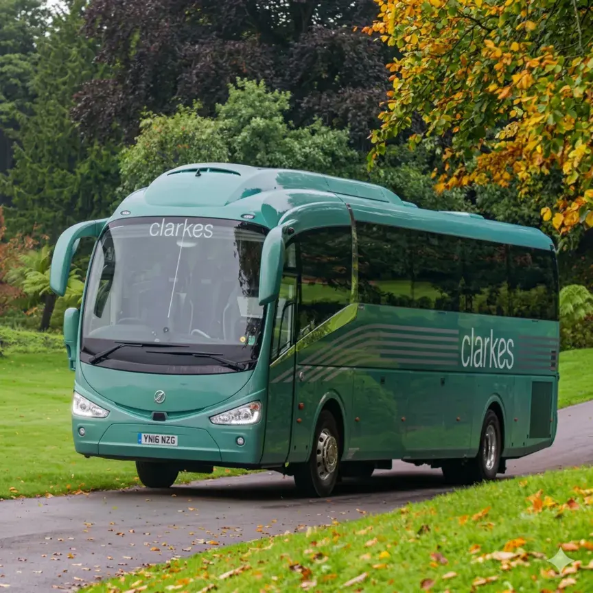 A photograph of a teal-green luxury coach with "Clarkes" branding on the side, seen from a front three-quarter view, parked on a paved driveway in a lush parkland setting with green grass and trees.